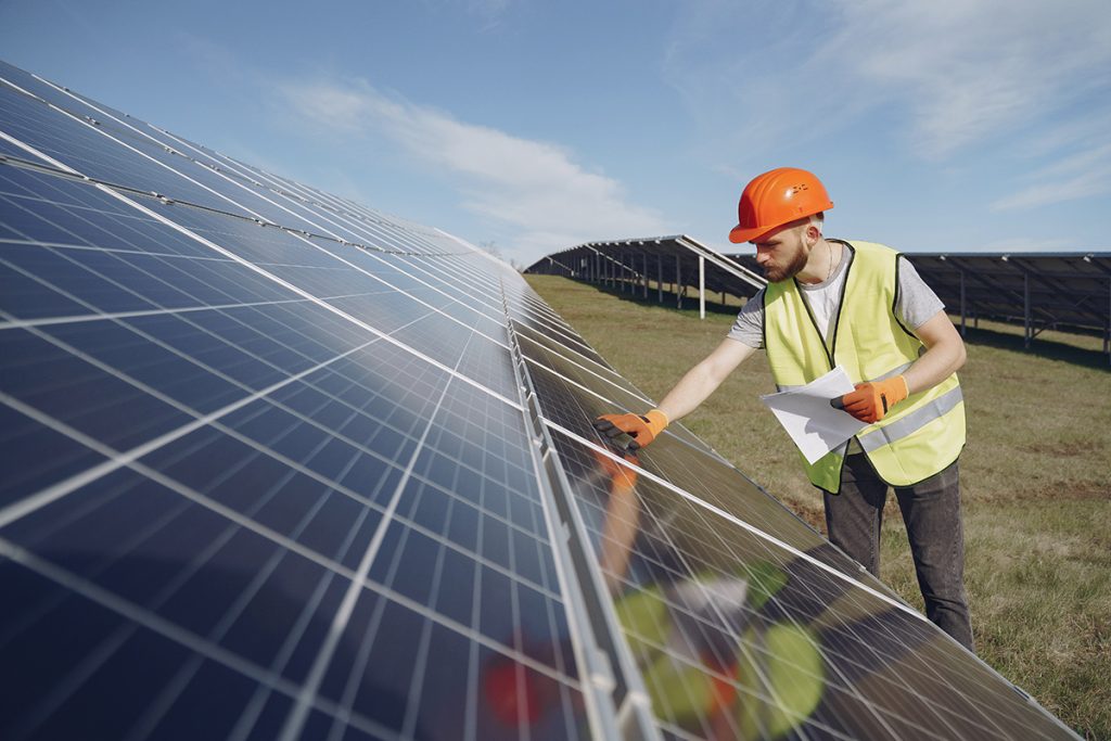 Man with hard hat reaching out and touching solar PV panels in a field