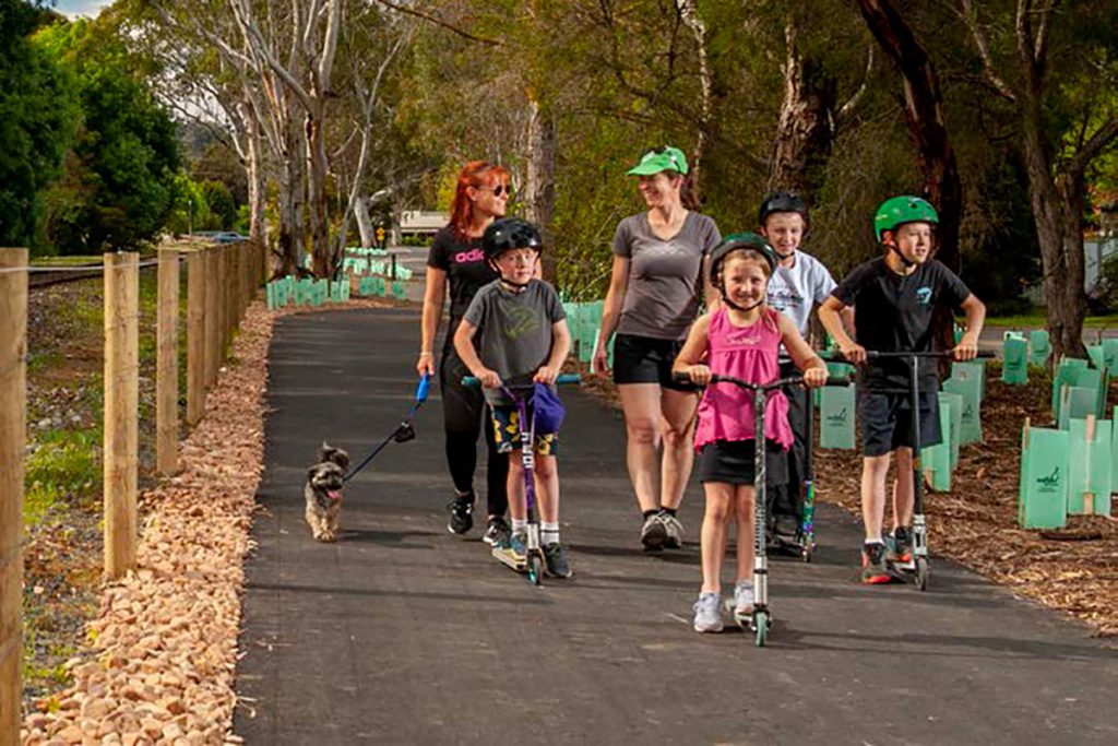 Family with dog and scooter on tree-lined walking trail