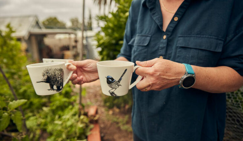 Person carry two cups of tea with gardens in the background